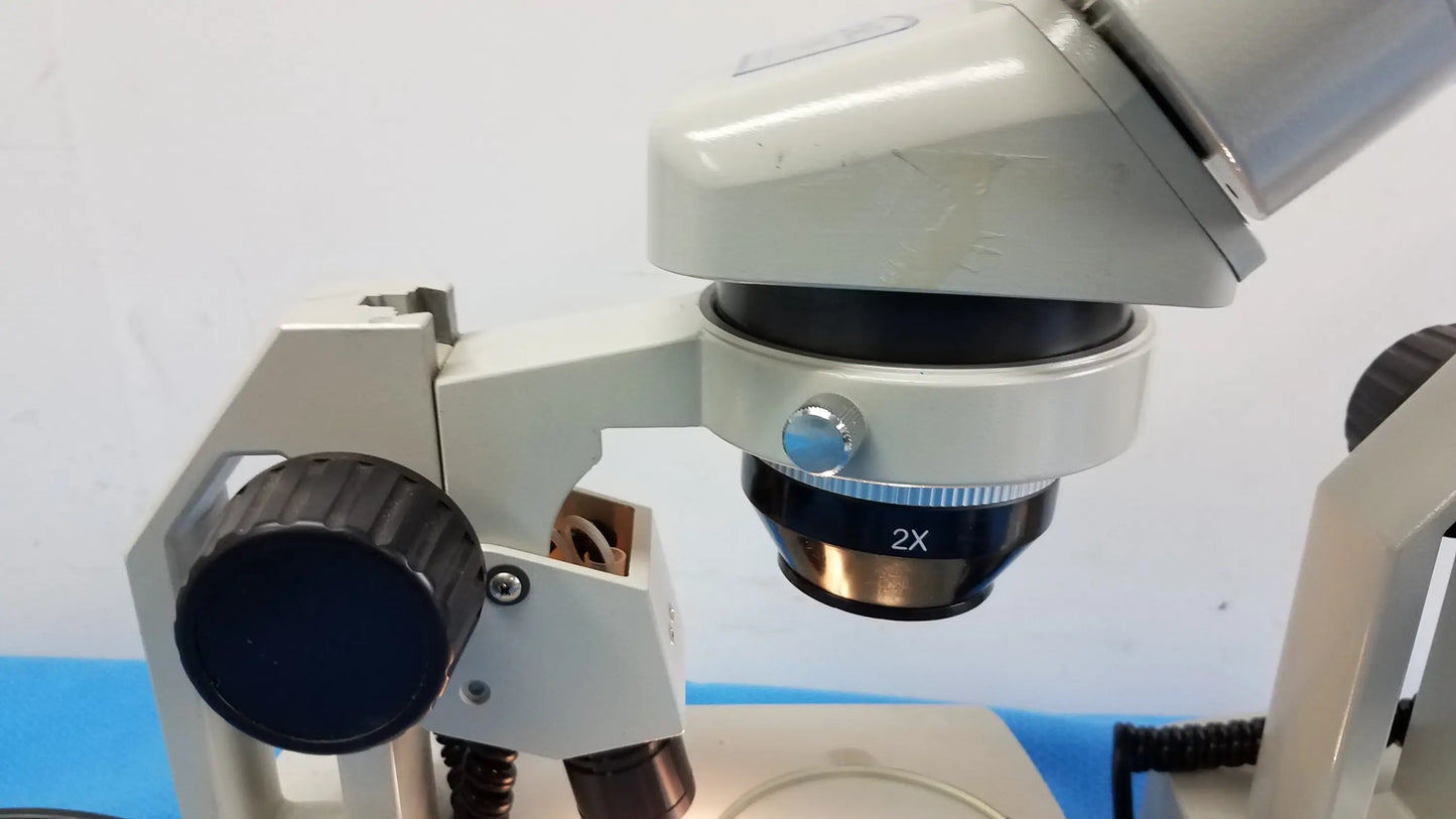 A white meiji techno stereo microscope with a black 2x objective lens and blue adjustment knob for medical equipment use