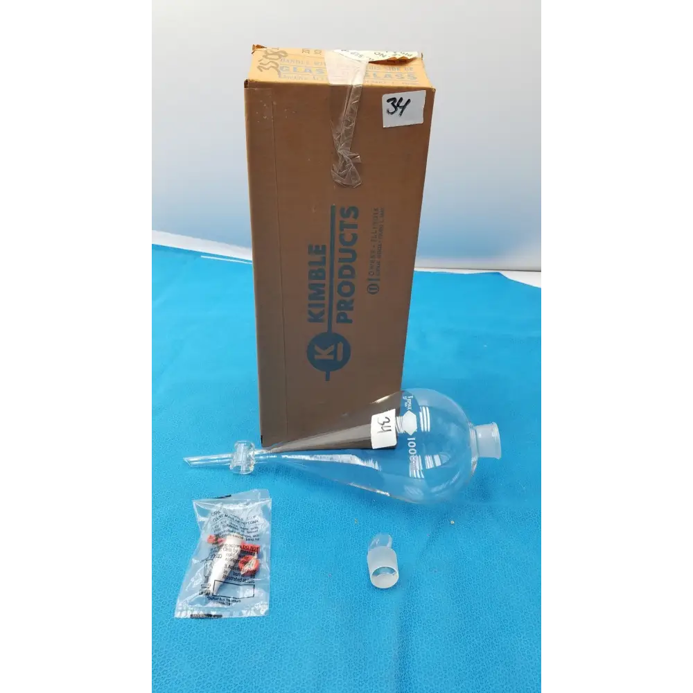 Clear glass kimble products 100 ml graduated volumetric flask with a narrow neck and bulbous body, marked with measurement lines.