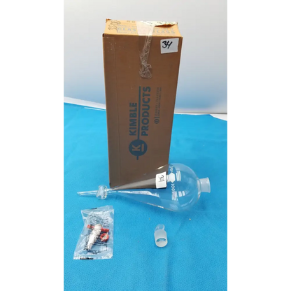 Clear glass kimble products 100 ml graduated volumetric flask with a narrow neck and bulbous body, marked with measurement lines.