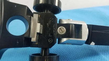 Adjustable flash gun bracket with black and silver metal microscope stage clamp and knurled adjustment knob for medical equipment