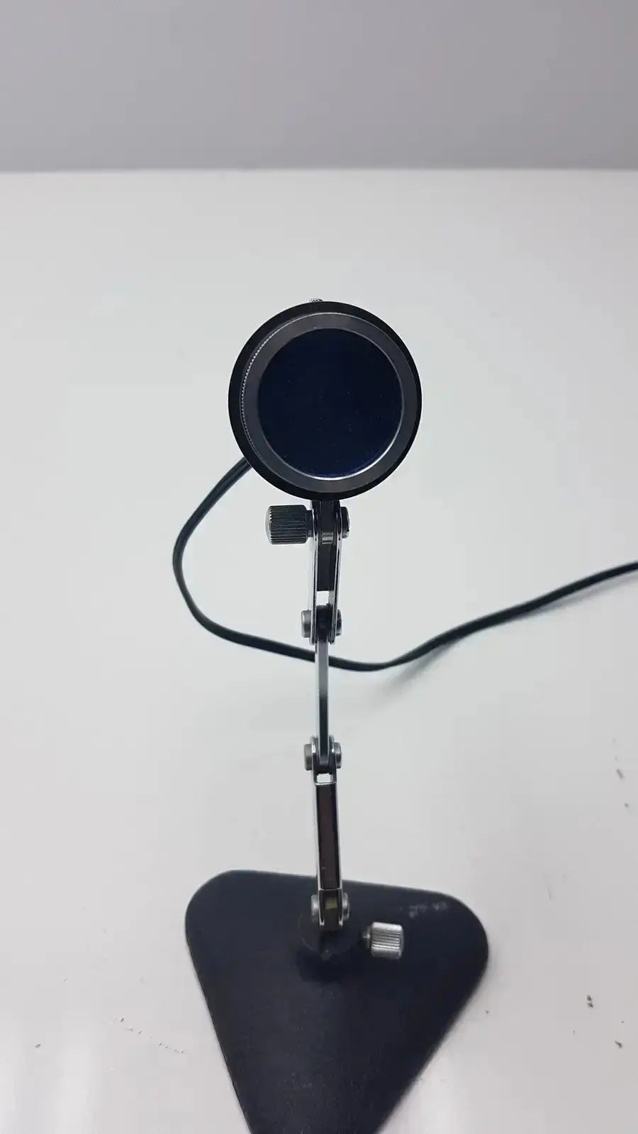 Black circular microscope illuminator light with a matte finish on an adjustable metallic stand for precise positioning