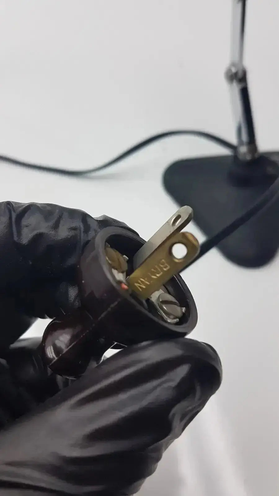 Black plastic electrical plug with brass prongs and brn marking on back side of adjustable microscope illuminator light lamp