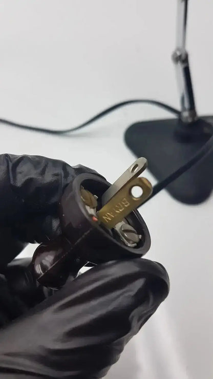 Black plastic electrical plug with brass prongs and brn marking on back side of adjustable microscope illuminator light lamp