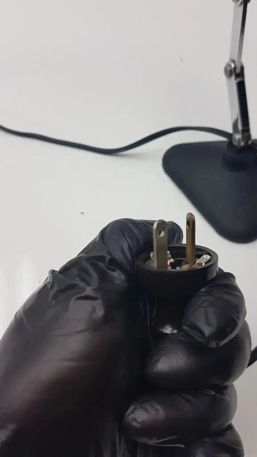 Black rubberized plug with two brass-colored prongs for adjustable microscope illuminator light lamp back side view