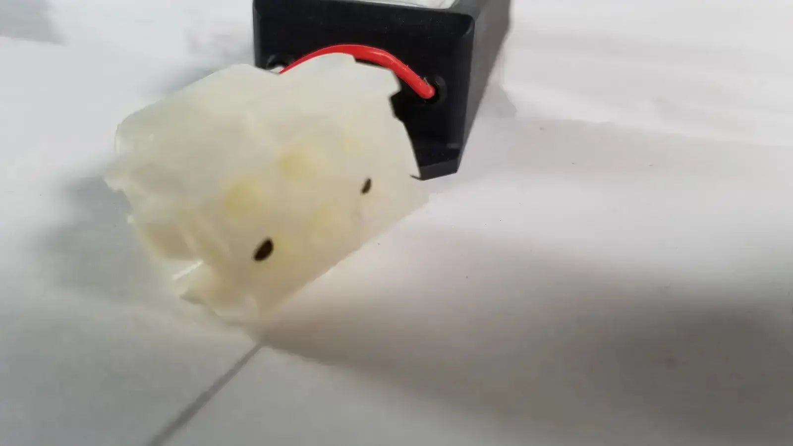 Off-white plastic light power supply with black indentations and red wire attached to black component for advanced sterilization products