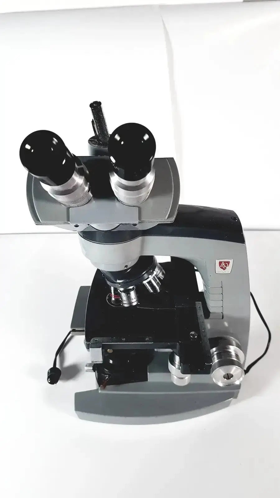 Gray and black American Optical Spencer microscope with dual eyepieces, metallic lenses, and sturdy base for precision use