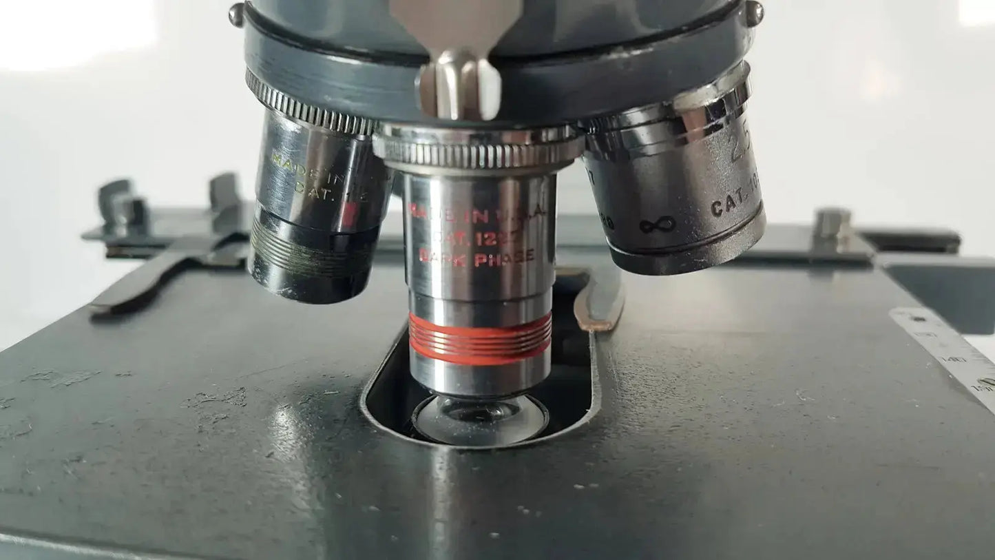 A metallic american optical spencer microscope objective lens with red ring and engraved markings on a dark gray stage