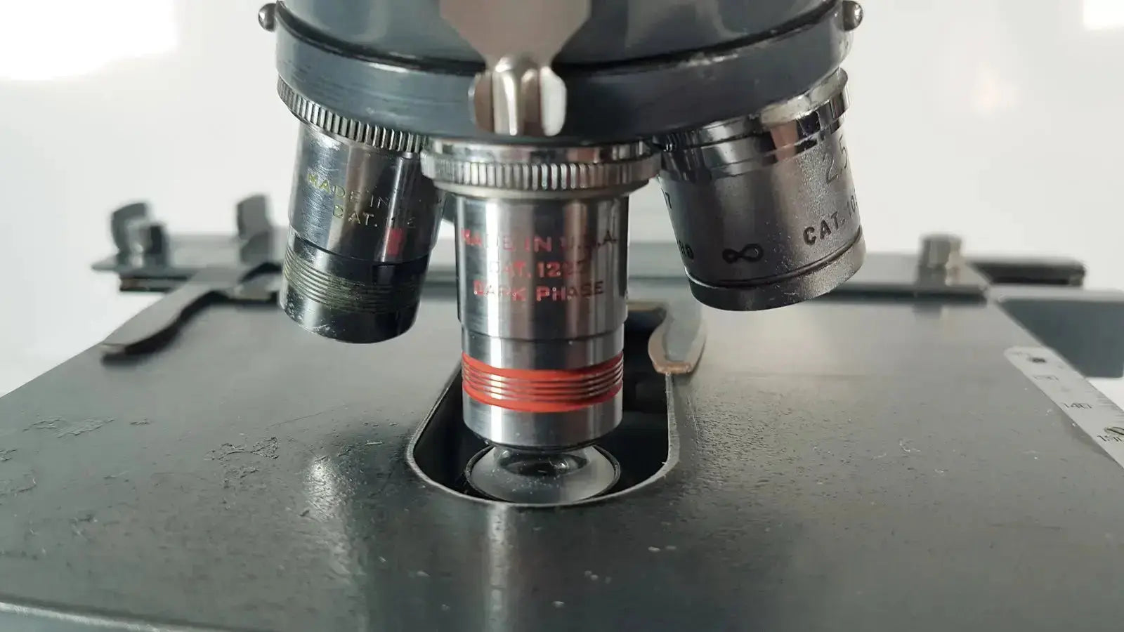 A metallic american optical spencer microscope objective lens with red ring and engraved markings on a dark gray stage