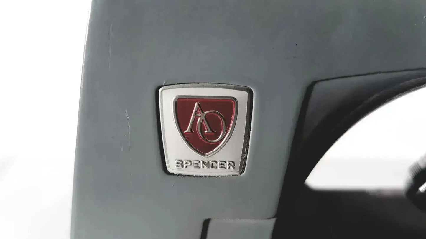 Silver and red shield-shaped emblem with ao insignia above spencer on gray surface of american optical spencer microscope
