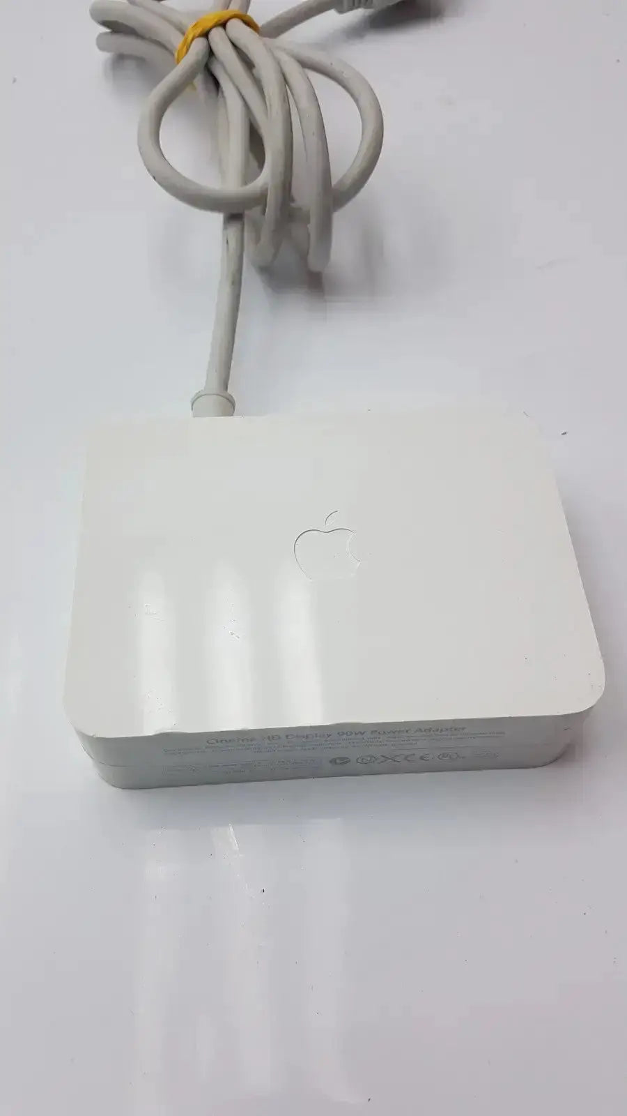 White Apple Cinema HD Display 90W power adapter with MagSafe 2 charger and coiled white power cable tied by yellow band