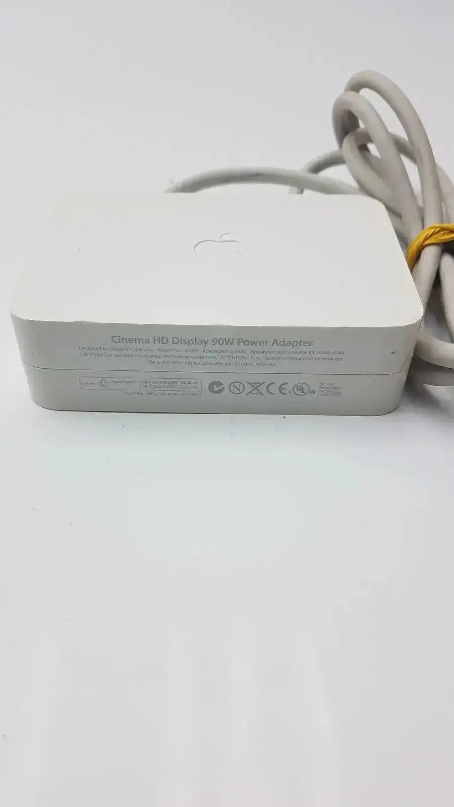 White rectangular Apple Cinema HD Display 90W power adapter with coiled gray cable tied by yellow band for reliable charging