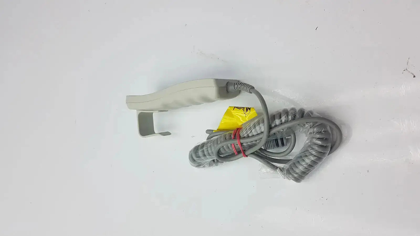 Gray coiled cable with beige-handled arjo huntleigh patient lift remote handset featuring yellow label and red tie