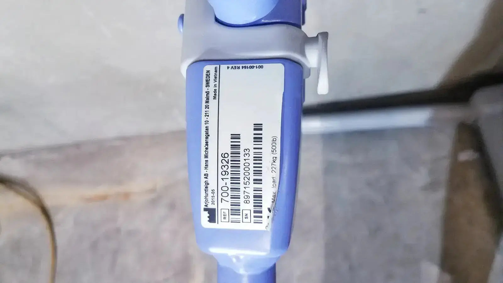 Blue and gray micro pipette with white label showing serial number and barcode on arjo maxi power patient lift handset