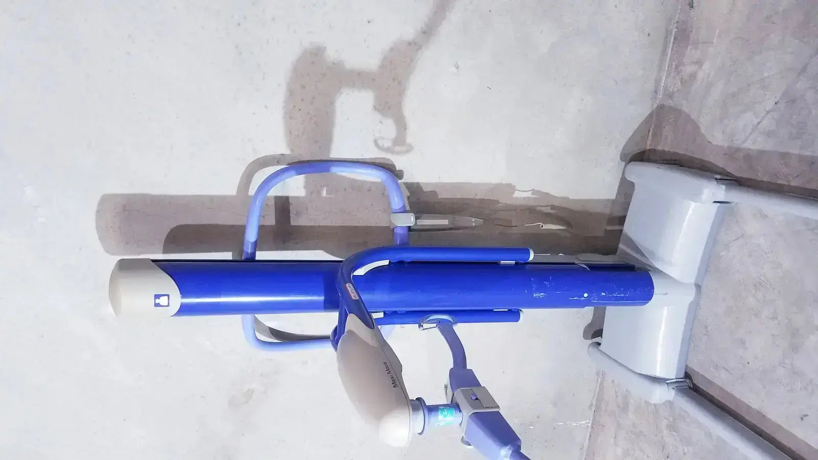 Blue and white public exercise bike with handlebars seat and pedals shown with arjo maxi power patient lift handset