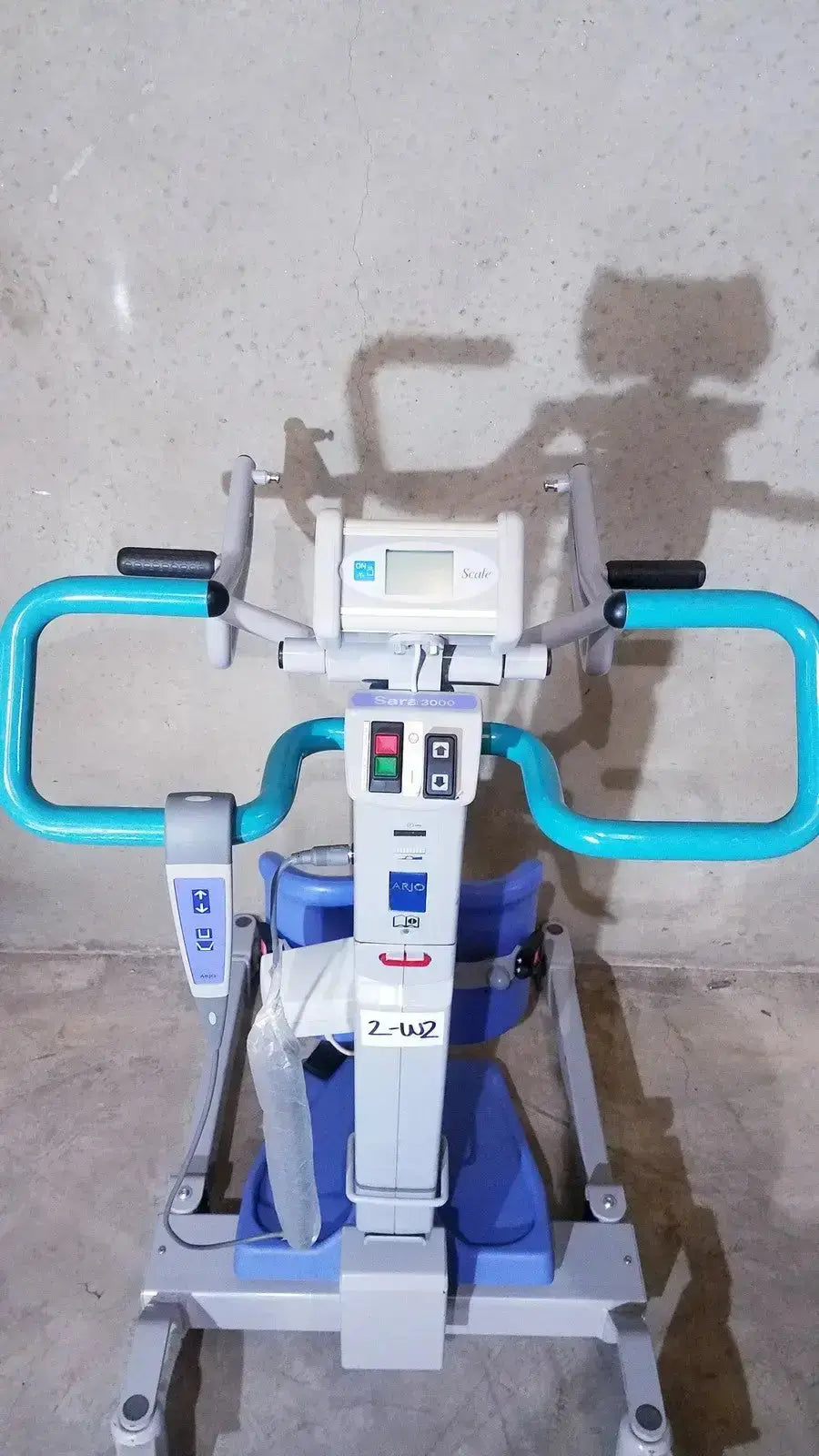 Blue and white arjo sara 3000 hospital mobile patient lift chair with control panel and handlebars for standing raising aid