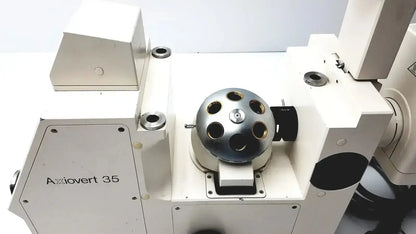 Silver metallic spherical component with circular apertures mounted on white axiovet 35 inverted phase contrast microscope