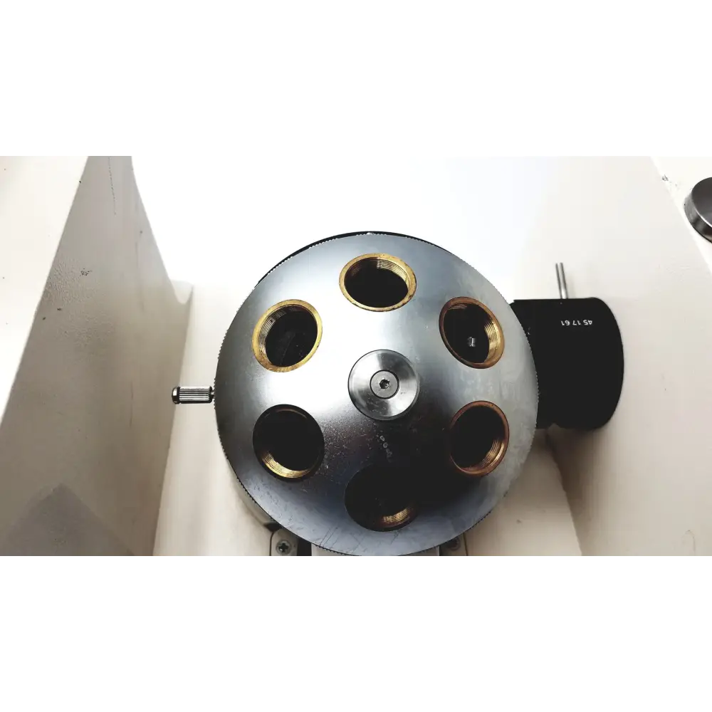 Silver metallic spherical device with six gold-ringed openings and a central screw, mounted on a white surface.