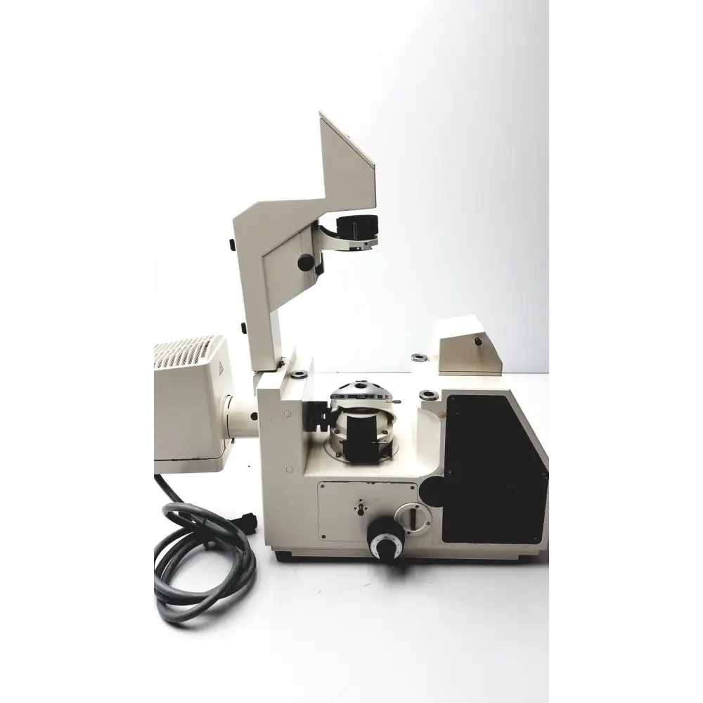 Beige and black scientific microscope with adjustable arm, stage, and objective lens turret.