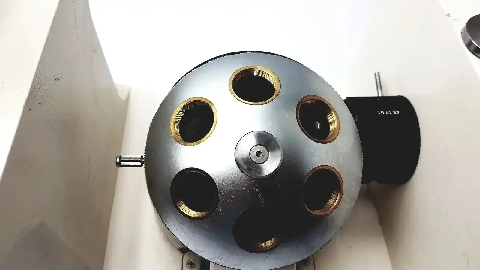 Silver metallic spherical device with six gold-ringed openings and central screw mounted on axiovert 35 inverted phase contrast microscope