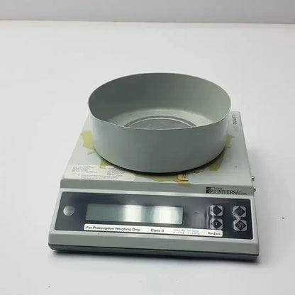 Gray metal weighing pan on a gray digital scale labeled hazel universal for baker universal prescription weighing g-box12-33i