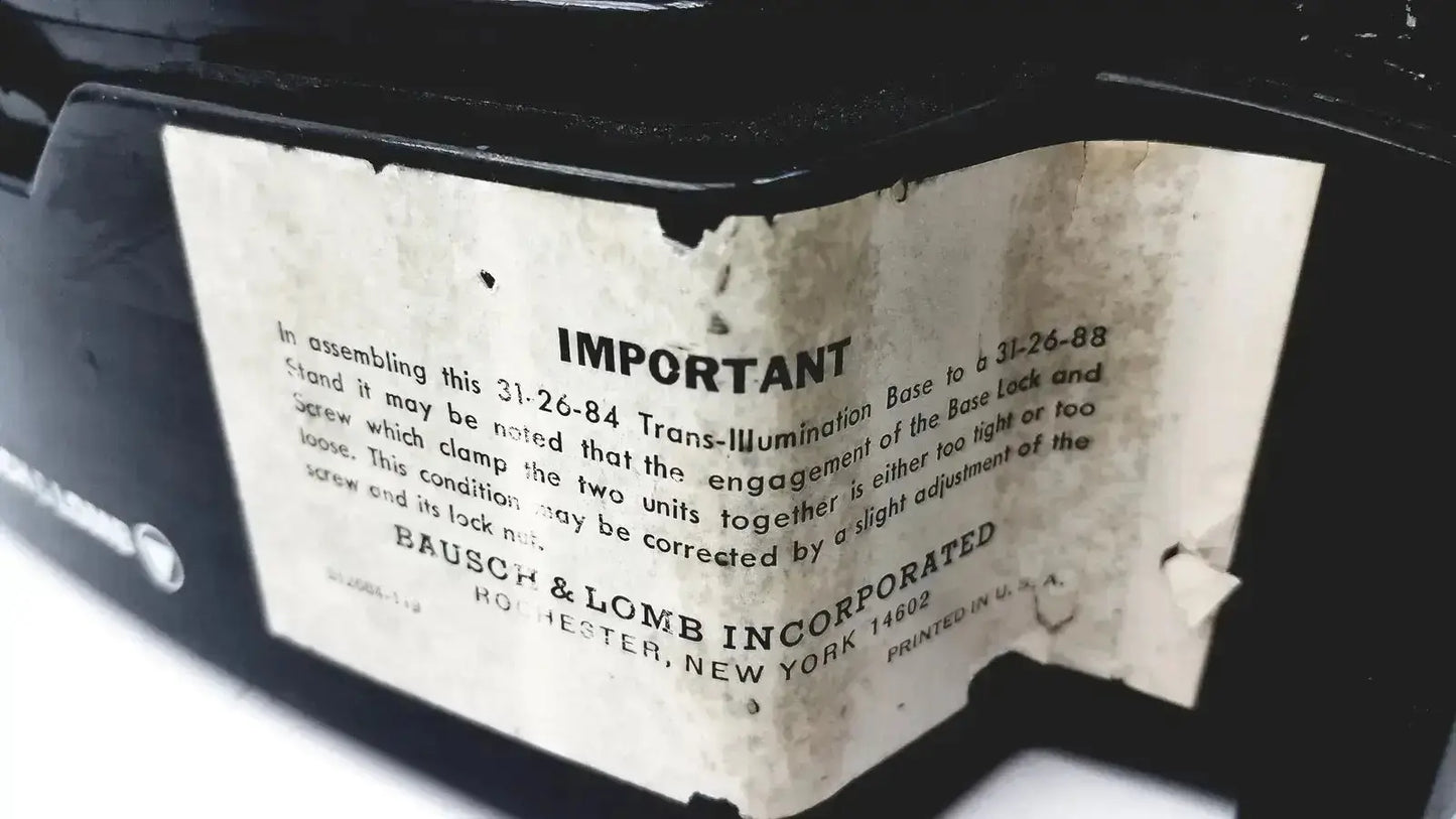 A weathered off-white paper label with black text and bausch & lomb incorporated branding on a lomb microscope for biomedical evaluation hospital surplus