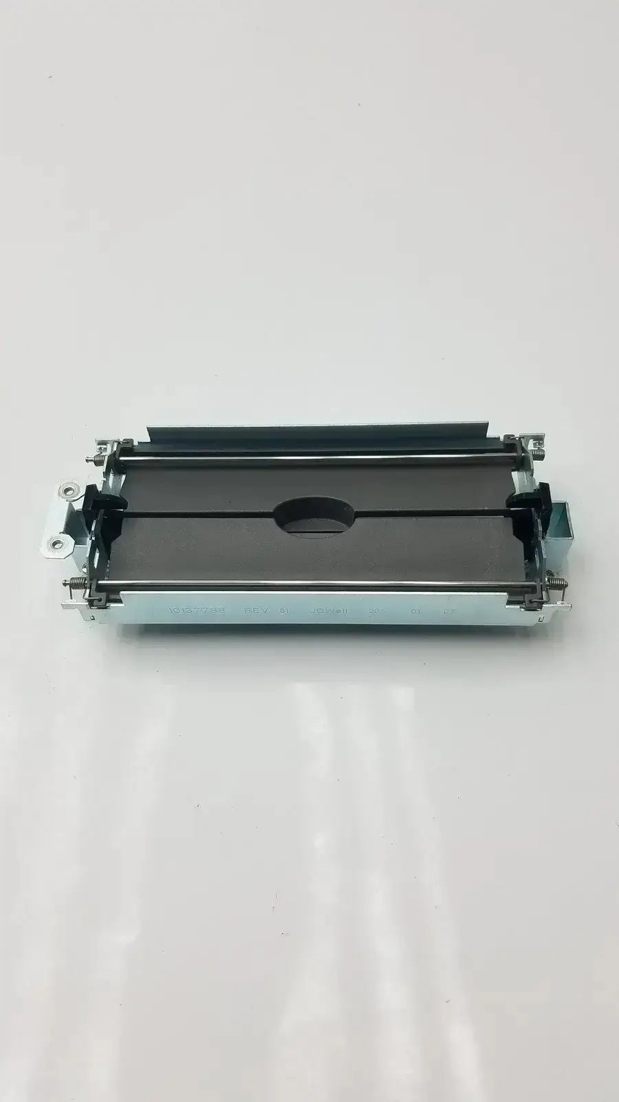 Silver-toned metal printer ribbon cartridge with black plastic parts and central oval cutout for assy secondary barrier