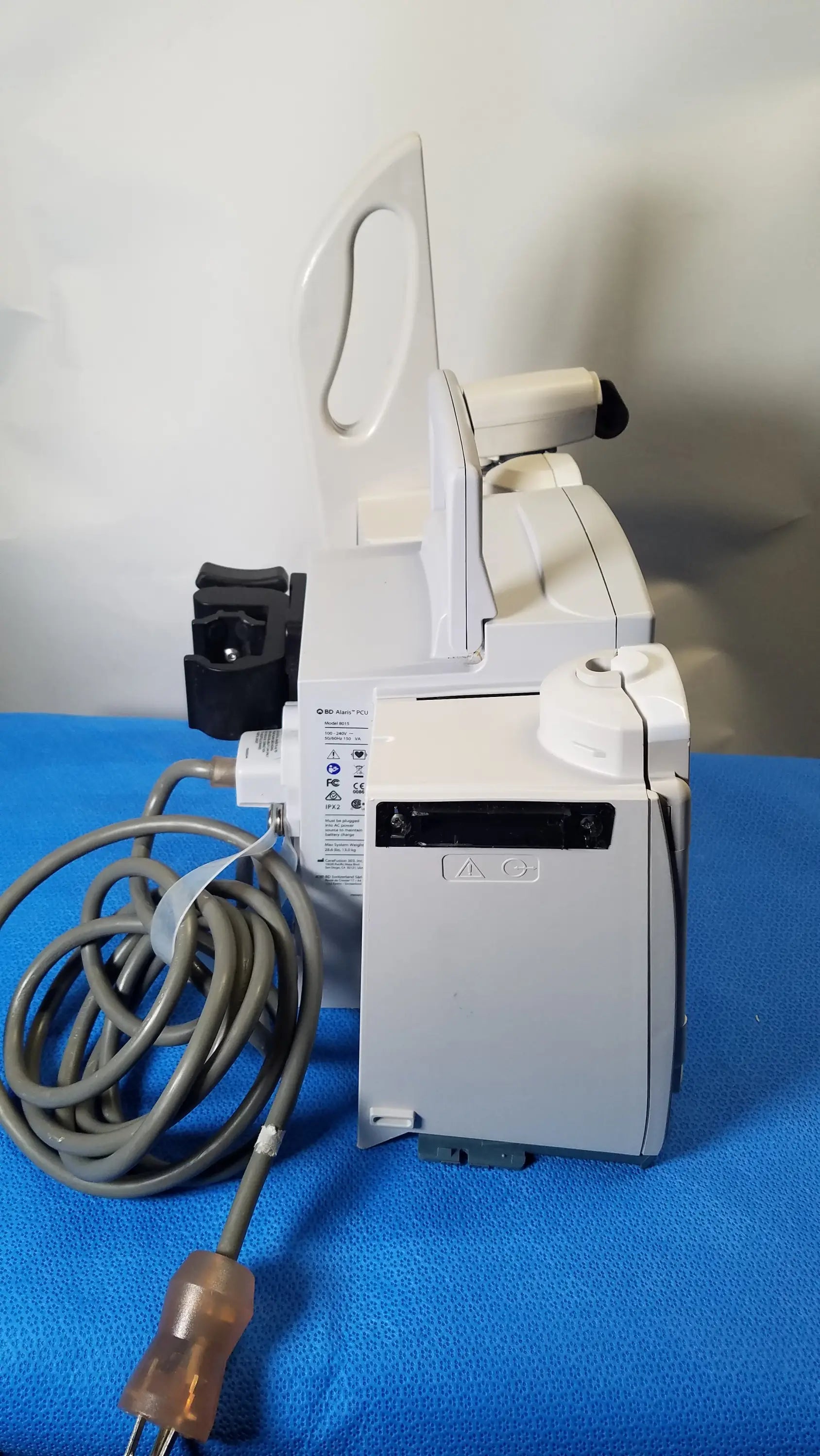 White BD Alaris 8015 PC modular infusion pump with 2x 8100 modules showing back side with coiled gray power cord in medical equipment use