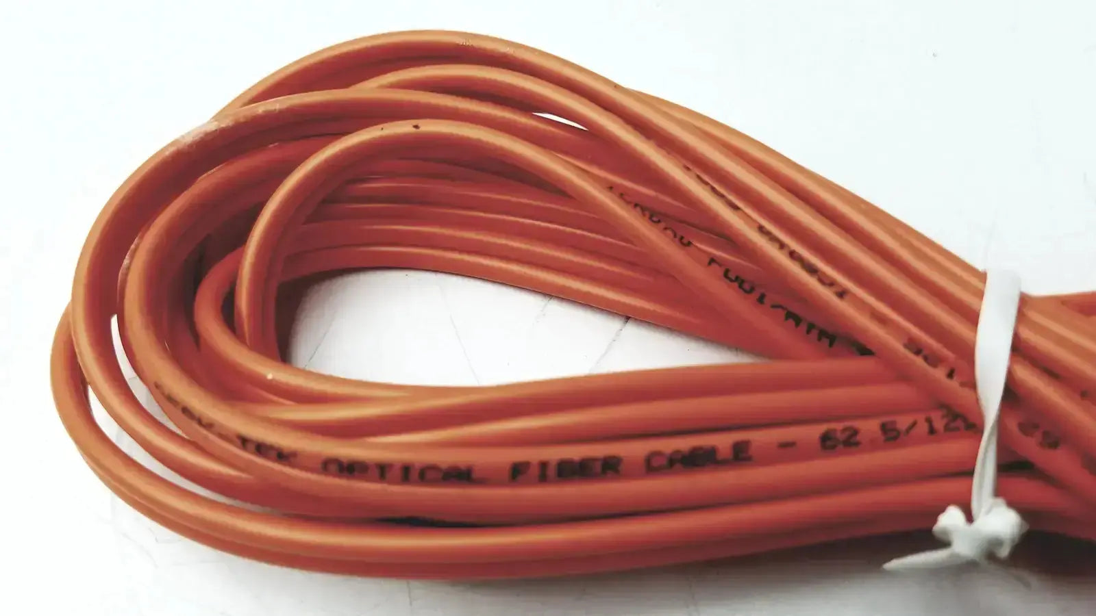 Orange coiled berk-tek optical fiber icr0x0 cable with black printed text and white zip tie from hospital surplus