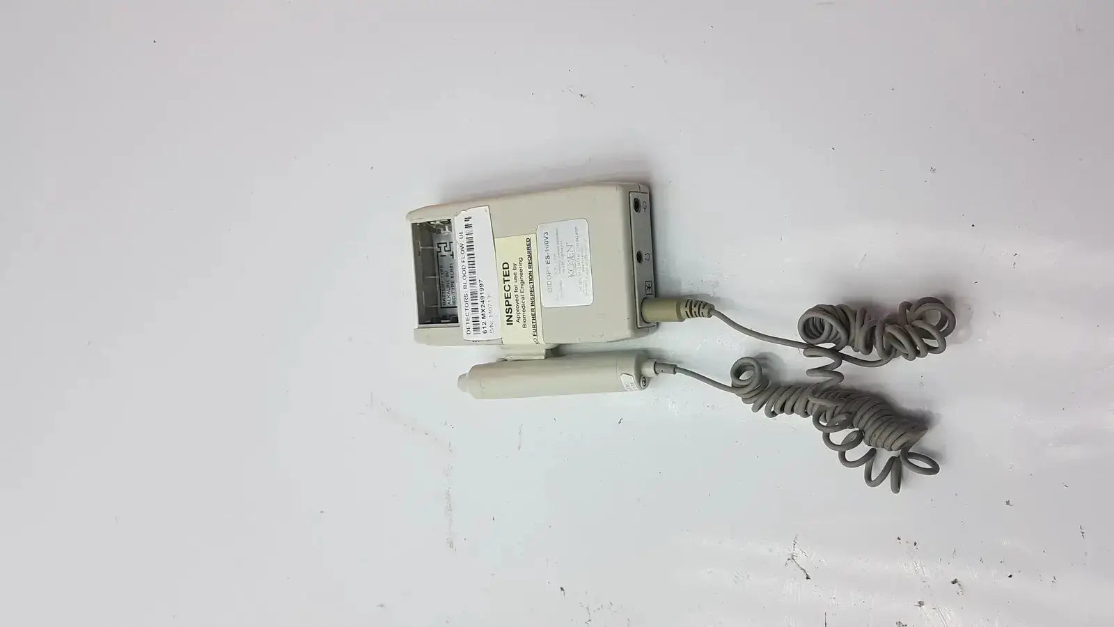 Beige plastic bi-directional vascular doppler handheld unit es-100v3 with coiled gray cables and unaccepted label visible