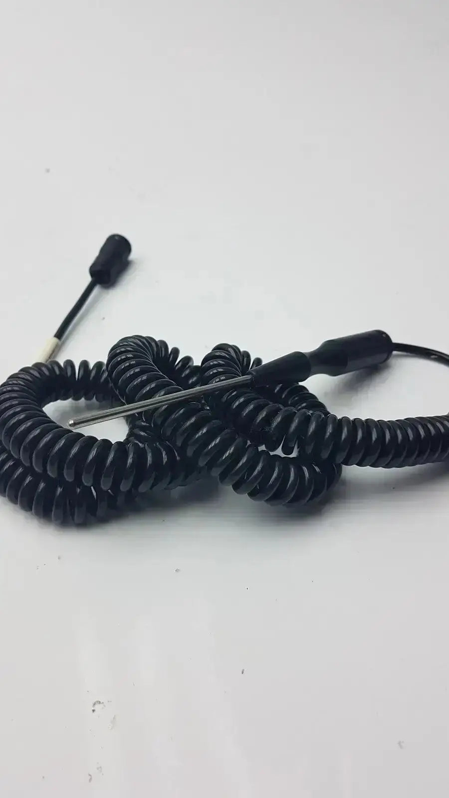 Black coiled thermometer probe with metallic tip and black connectors used by biomedical technicians from hospital surplus
