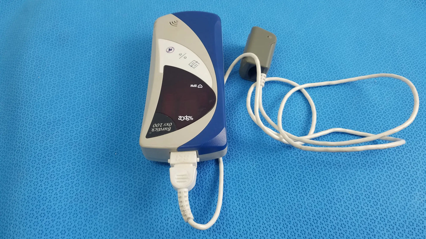 Blue and gray bionik ort-100 medical equipment with usb cable connected showing back side of burdick oxy 100 pulse oximeter ref 92521