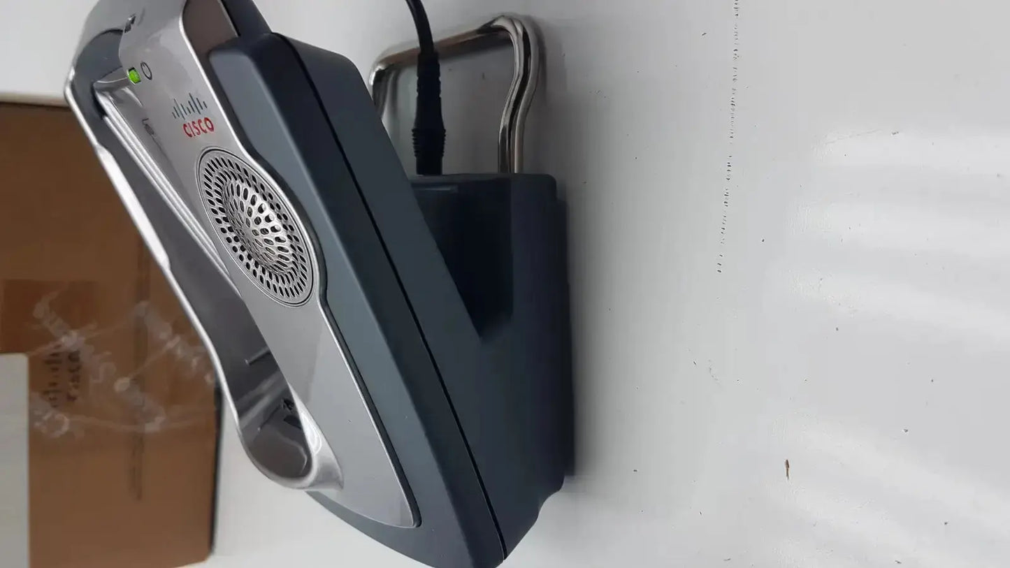 Silver and black cisco cp-7921g-a-k9 wireless ip phone mounted on wall with circular speaker grille and base box