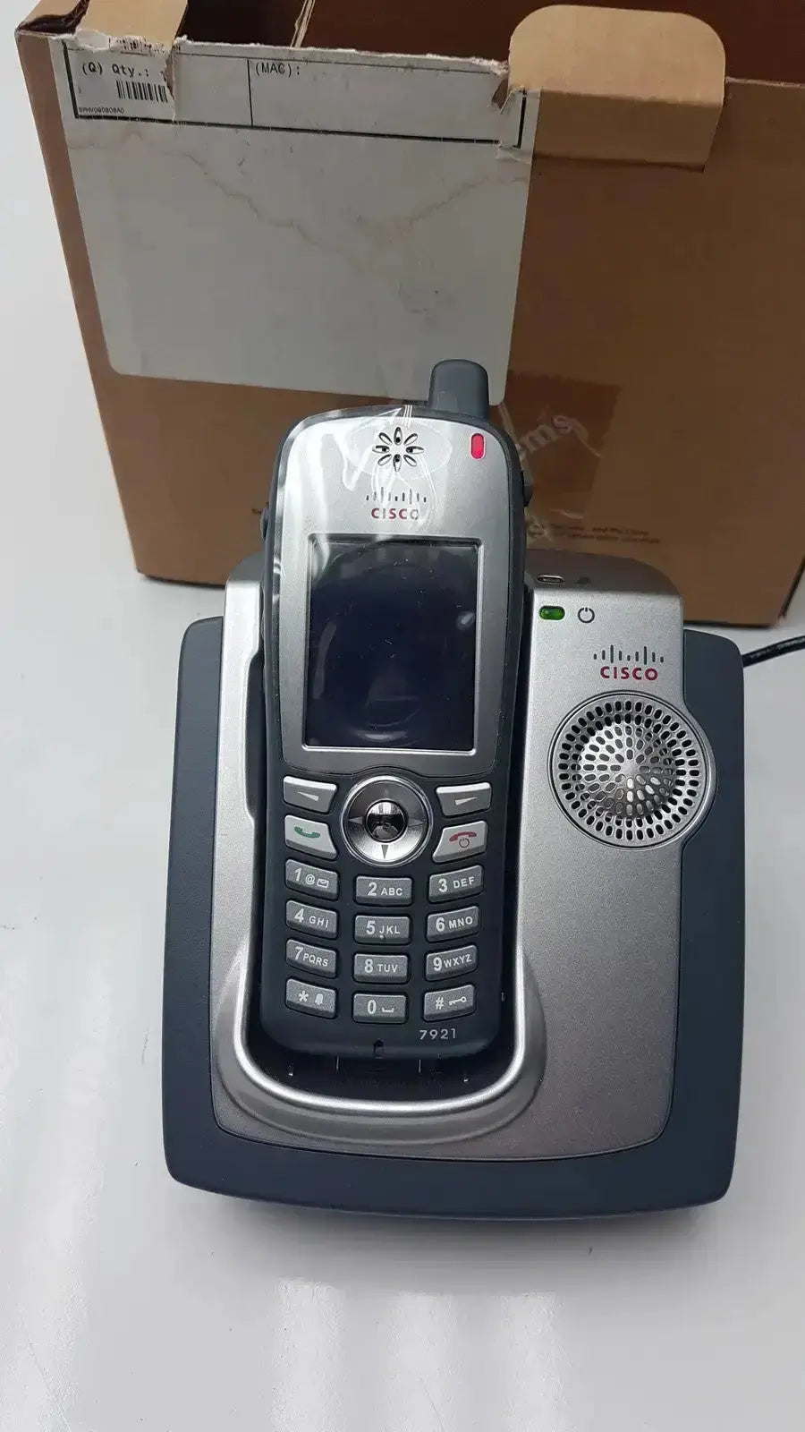 Silver cisco cp-7921g-a-k9 wireless ip phone with numeric keypad and antenna resting on matching charging base