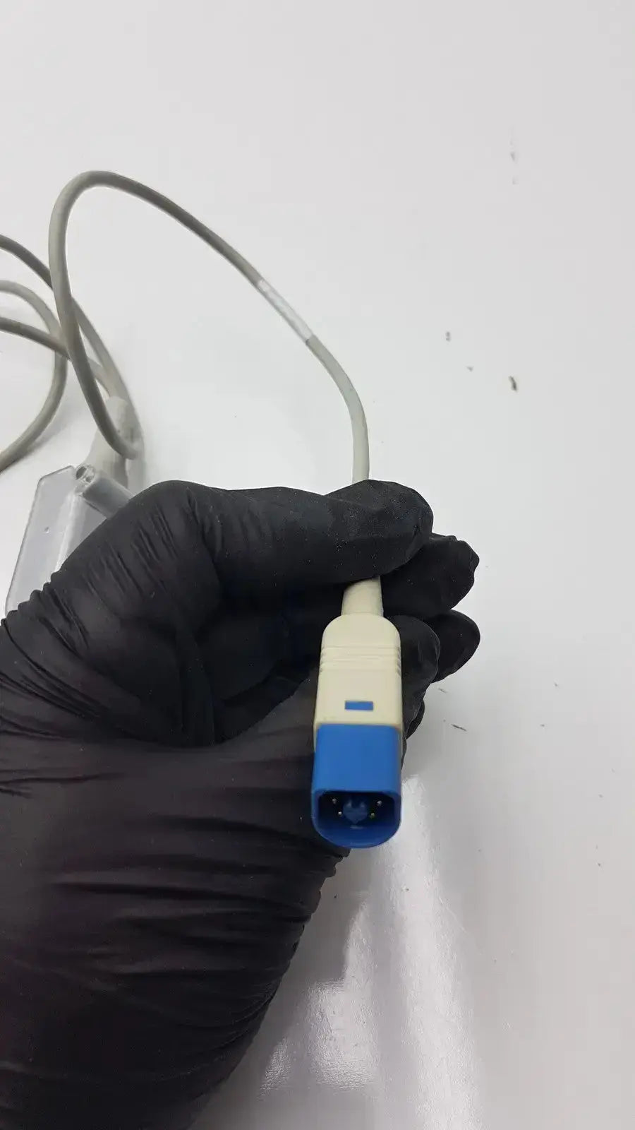Blue and beige compatible drager spo2 extension cable held in gloved hand for spo2 sensor connection