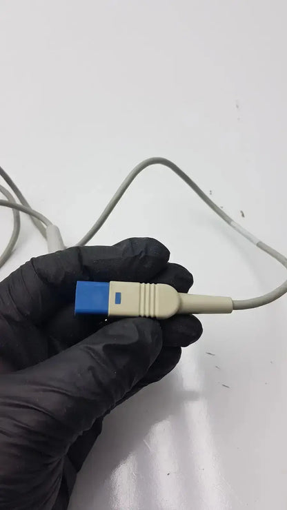 A beige and blue medical-grade compatible drager spo2 extension cable connector held in a gloved hand