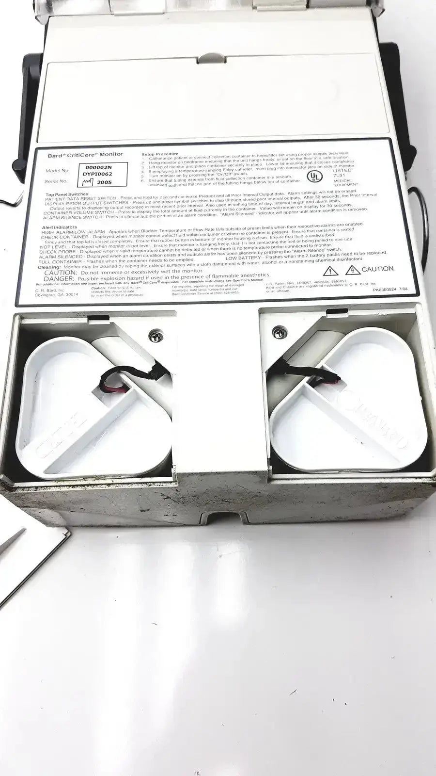 White plastic box containing two black circular components of criticore fluid output and temperature monitor model 000002n