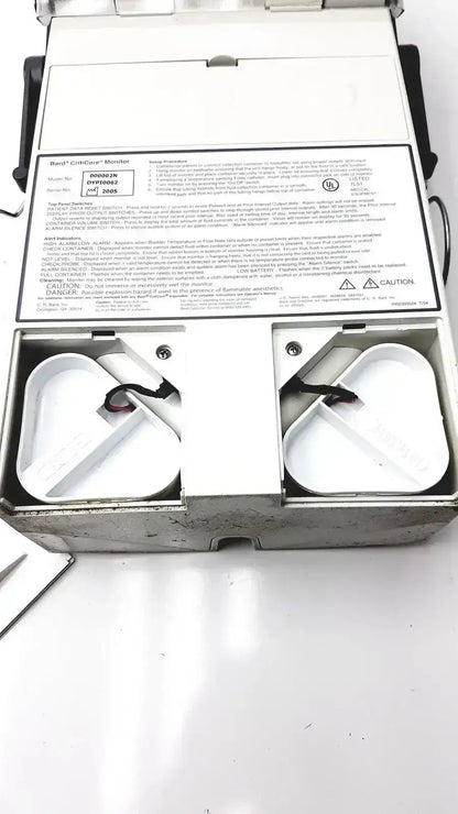 White plastic box containing two black circular components of criticore fluid output and temperature monitor model 000002n