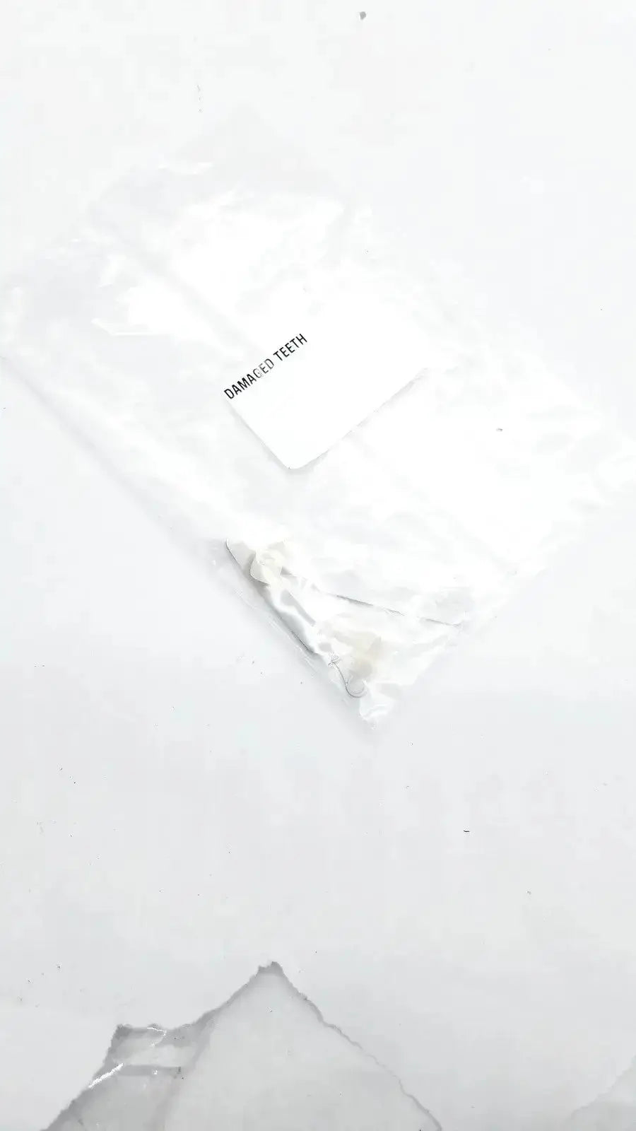 A white translucent plastic bag containing a small metallic dental appliance labeled damaged teeth for damaged teeth portrait ipn