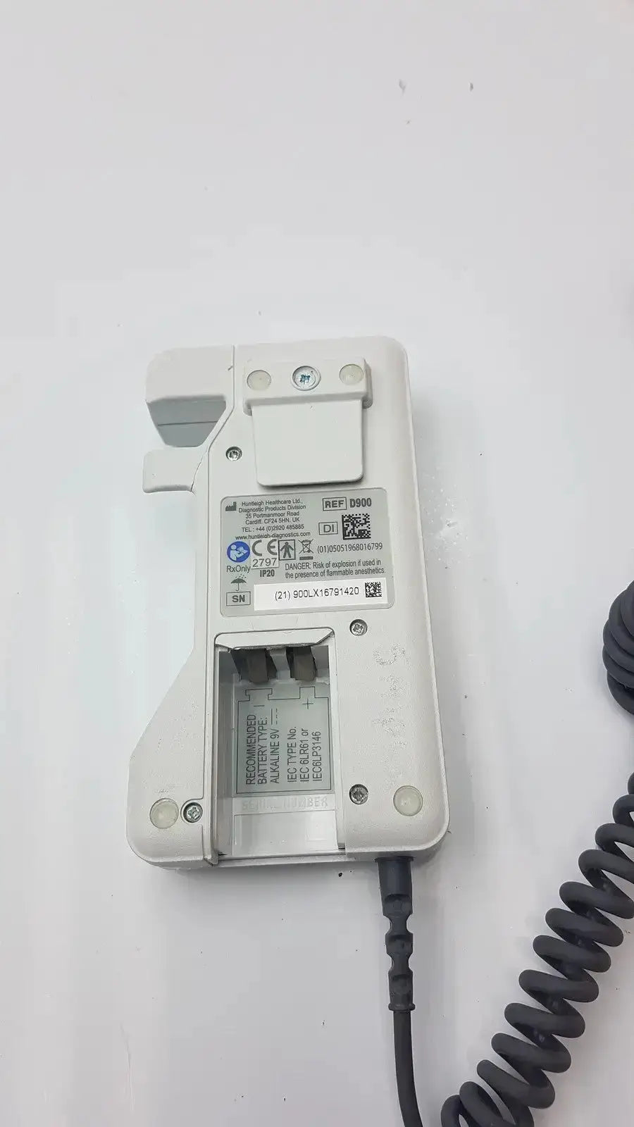 White plastic doppllex d900 handheld portable doppler showing coiled black cable and battery compartment label on back side