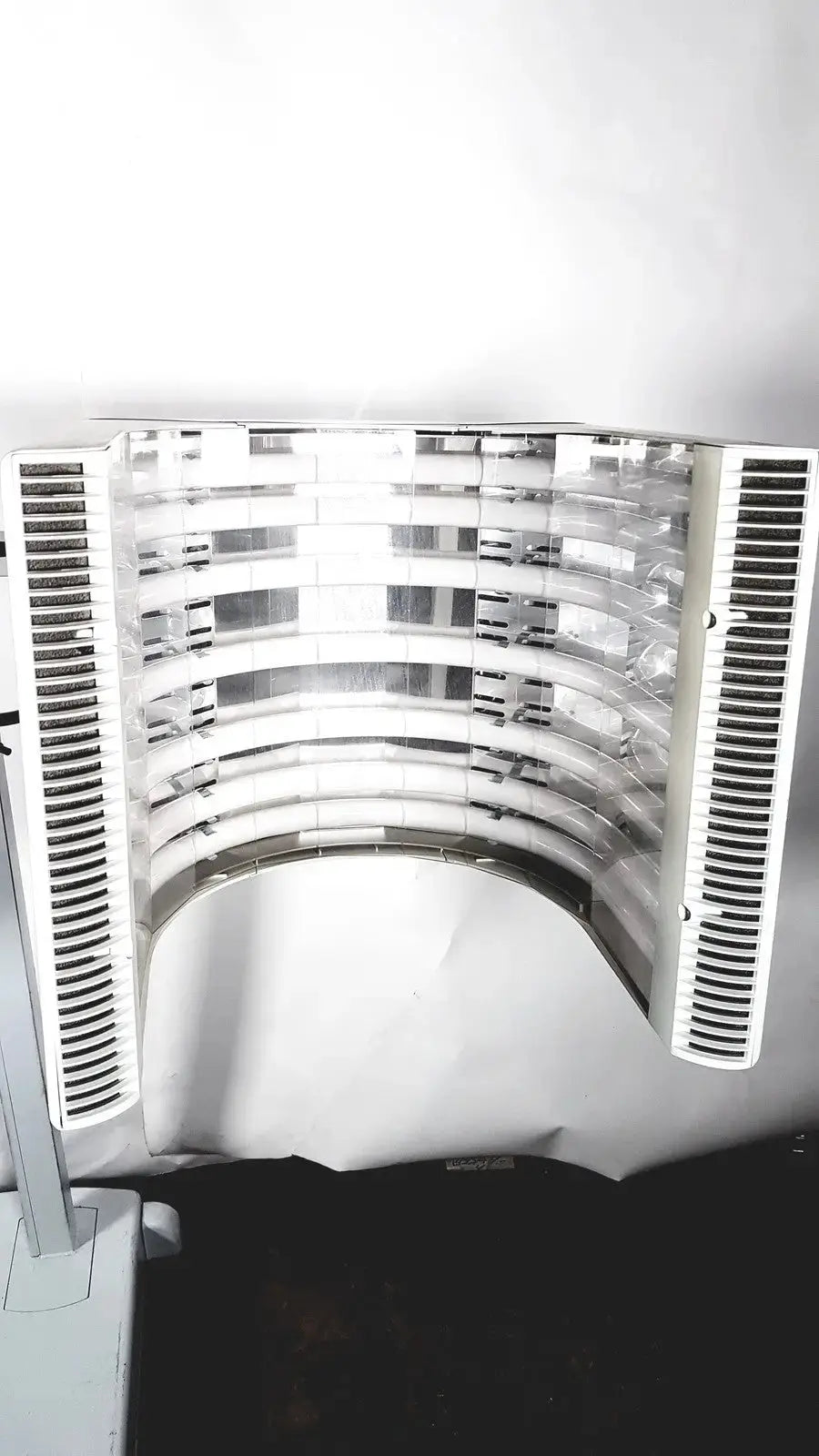Curved white plastic air vent with horizontal slats and central transparent panel on dusa blu blue light photodynamic therapy system