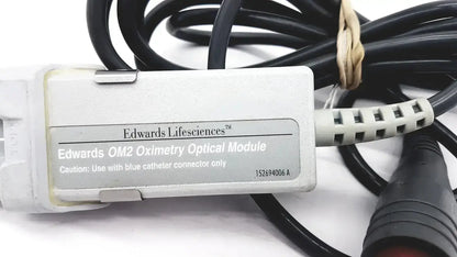 White plastic Edwards Lifesciences OM2 oximetry optical module cable adapter with black coiled cables and beige tie