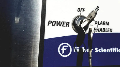 A silver key inserted into the circular lock of a white and blue Fisher Scientific isotemp laboratory freezer refrigerator
