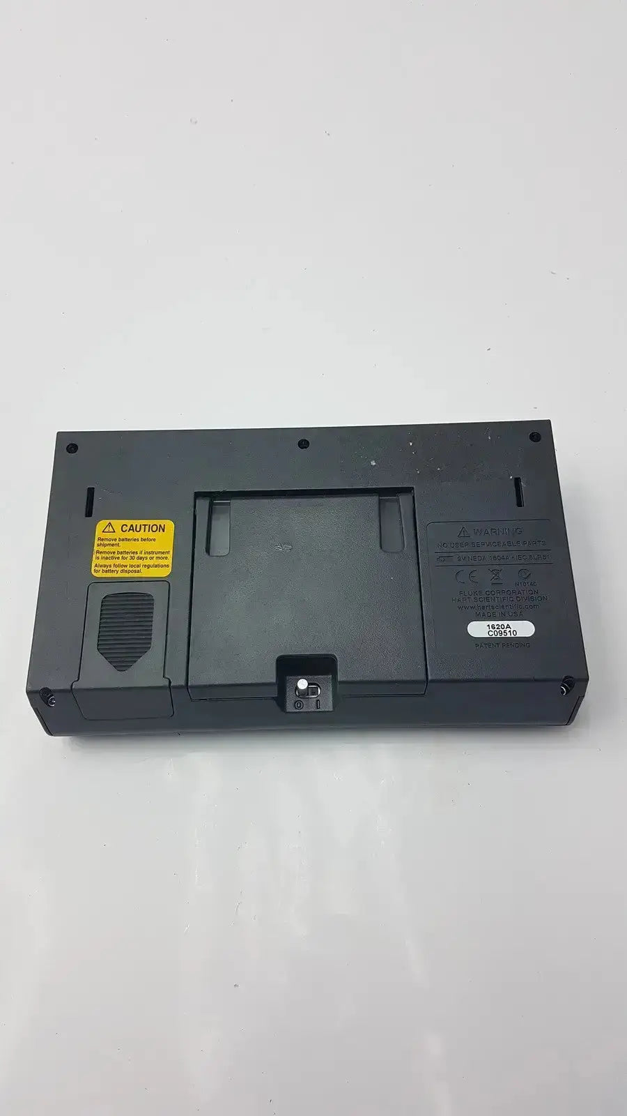 Black plastic laptop battery with yellow caution label and serial sticker on the back of fluke 1620a dewk digital thermometer