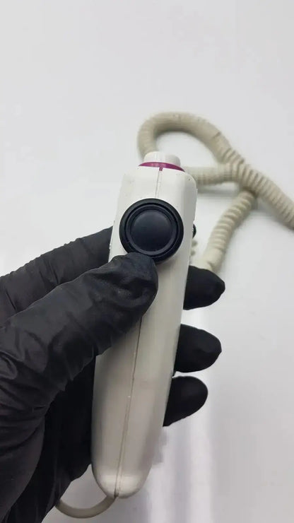 White handheld dragonfly hand switch with black circular button and coiled beige cable for medical use