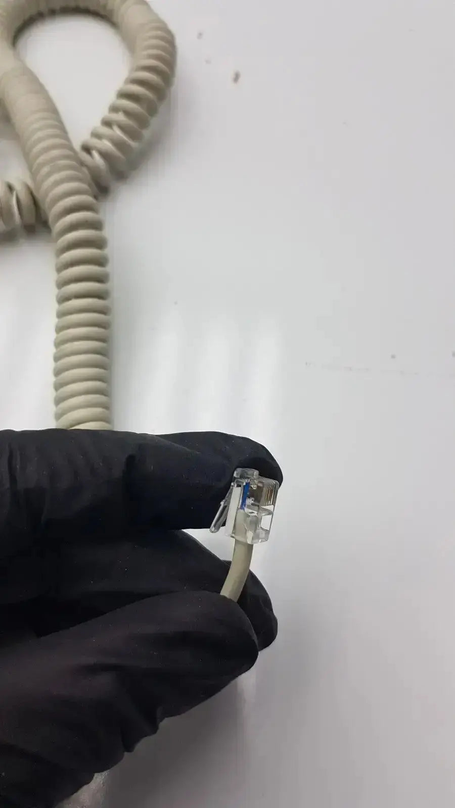 A beige coiled telephone cable with a clear rj45 connector held by black-gloved hands for the dragonfly hand switch