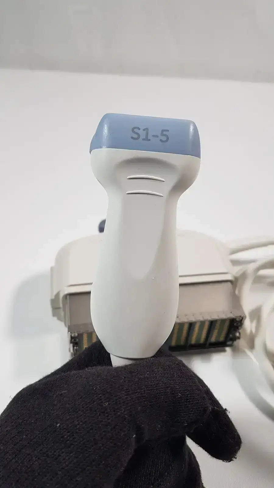 Ge s1-5-d phased array ultrasound probe in white and light blue held in black-gloved hand for medical imaging