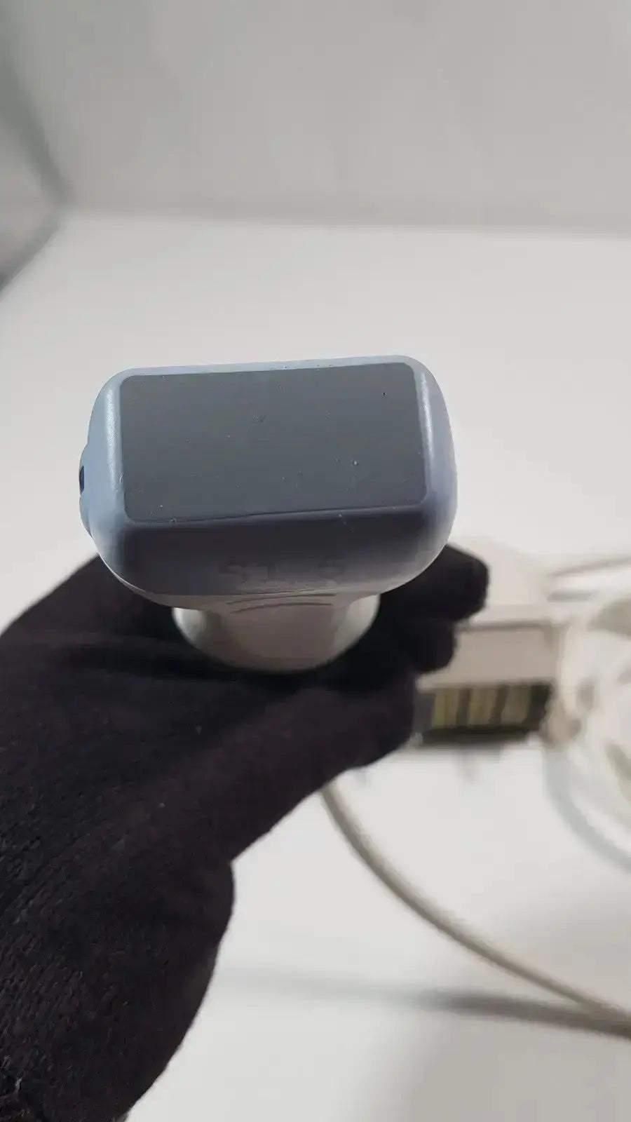 Gray plastic handheld barcode scanner with white base held in black-gloved hand for s1-5-d phased array ultrasound probe use