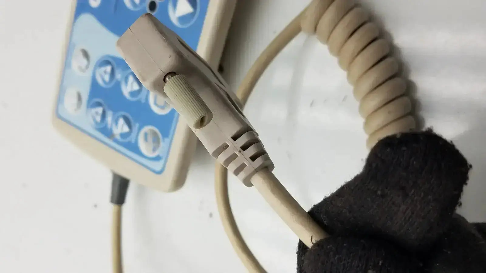 Beige coiled patient hand control cable with molded connector attached to blue and beige Hill-Rom bed control panel