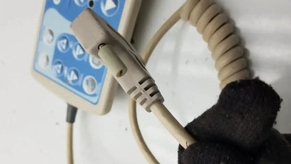 Beige coiled patient hand control cable with molded connector attached to blue and beige Hill-Rom bed control panel