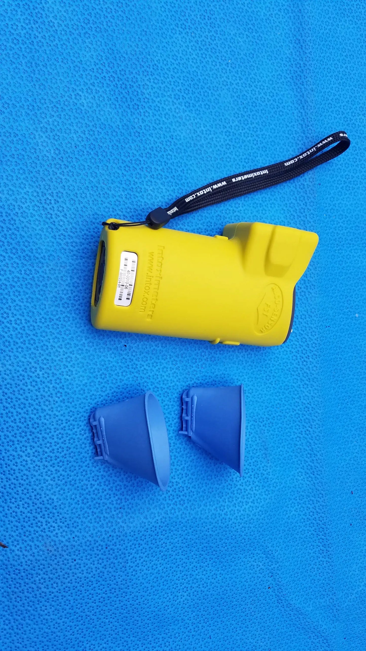 Yellow plastic pepper spray device with black wrist strap and two blue caps alongside intoximeters alco-sensor fst medical equipment case